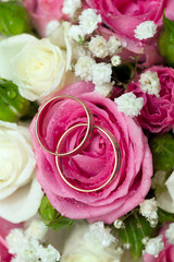 Gold wedding rings of the groom and the bride on a bunch of flow