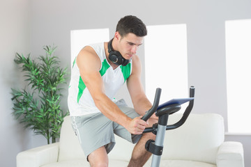 Obraz na płótnie Canvas Sporty handsome man training on exercise bike using tablet