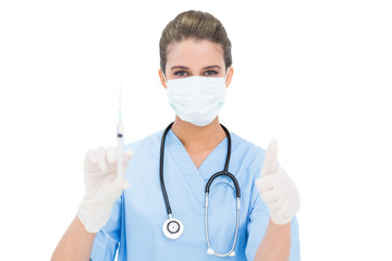 Beautiful brown haired nurse in blue scrubs holding a syringe an