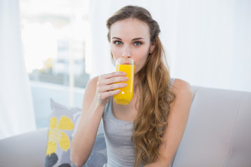 Content young woman sitting on sofa drinking glass of orange jui