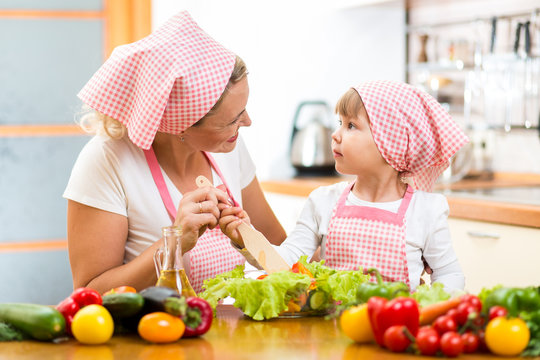 mother teaching kid daughter mixing salad at kitchen