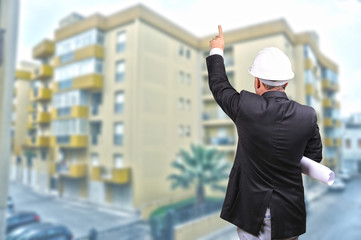 Bauarbeiter mit Planrolle deutet auf hochhaus