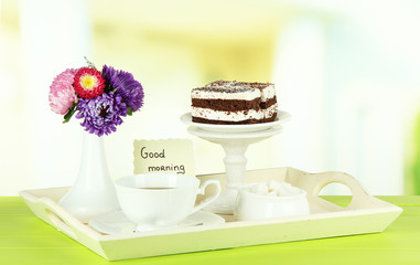 Cup of tea with cakes on wooden tray on table in room