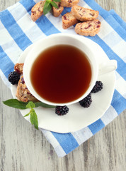 Cup of tea with cookies and blackberry on table close-up