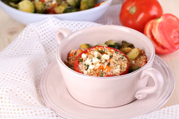 Stuffed tomatoes in pan and bowl on wooden table close-up