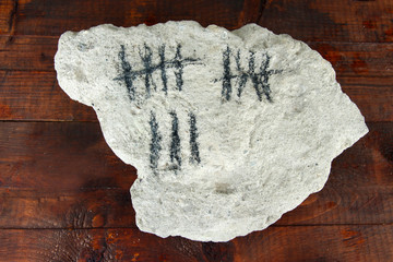 Counting days by drawing sticks on stone on wooden background