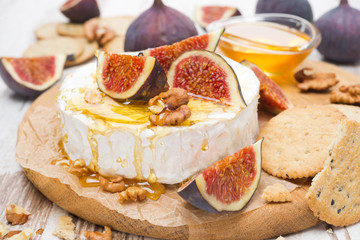 Camembert cheese with honey, figs and crackers on a wooden board