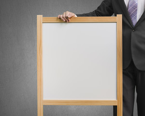 Businessman hold wooden white blank board in gray concrete backg