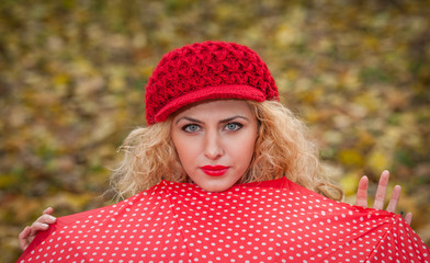 Attractive blonde girl with red cap looking over red umbrella
