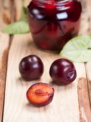 Plums on rough wooden table. In background glass jar with jam.