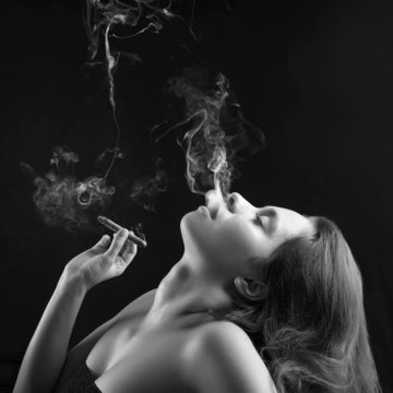 Woman smoking cigar against dark background. Black and white stu