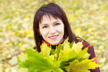 portrait of smiling woman with maple leaves in autumn