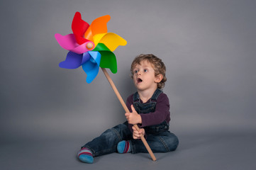 Young kid portrait with windmill over grey background.