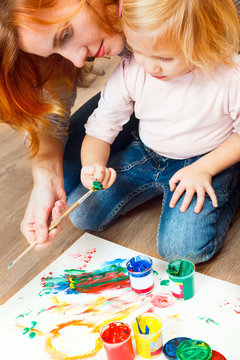 Cute little redhead girl painting with mother.