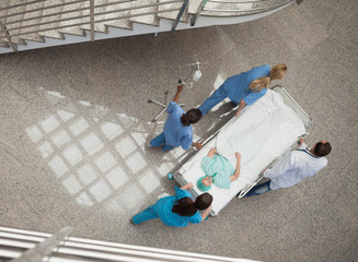 Three nurses and one doctor pushing a patient in a gurney - obrazy, fototapety, plakaty