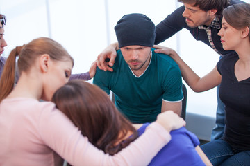 Several people comforting young man on background.