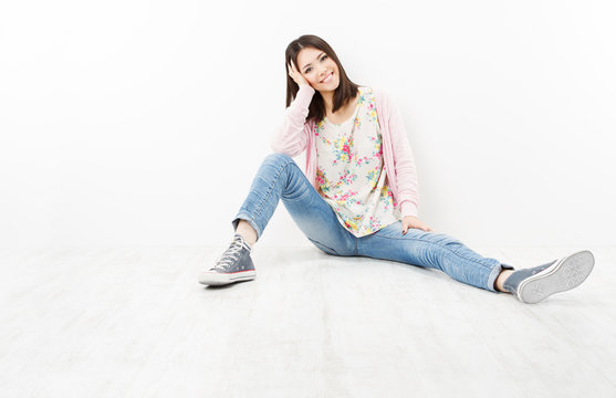 Young woman teenager in jeans sitting on white floor