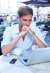 Handsome young man with laptop and cup in a summer cafe