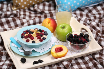 Oatmeal in plate with berries on napkins on wooden tray on bad