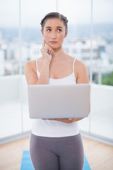 Thoughtful sporty brunette using her laptop