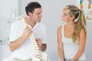 Smiling physiotherapist showing patient something on skeleton mo