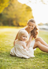 Fototapeta premium Happy mother and baby sitting on meadow in park