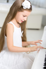 Portrait of little girl in white dress playing piano