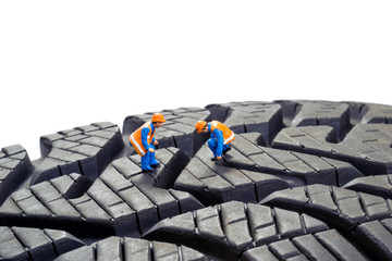 Miniature workers checking the depth tread on a car tyre