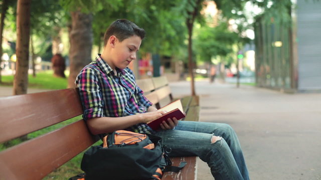 Young boy reading book on bench in the city