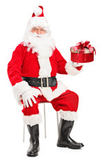Smiling Santa Claus on a chair holding a present