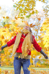 Happy woman throwing autumn leaves in the park.