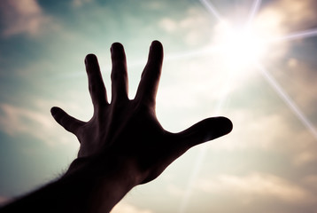 Hand of a man reaching to towards sky. Color toned image.