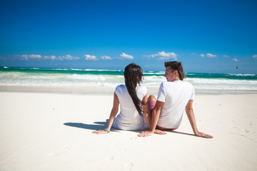 Fototapeta premium Back view of young couple in love sitting at tropical white