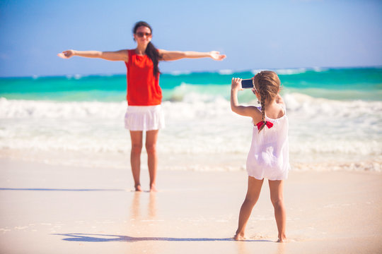 Little girl photographs her mother on the beach