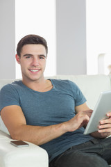 Cheerful handsome man relaxing on couch using tablet