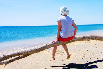 Woman sitting on beach in tree trunk