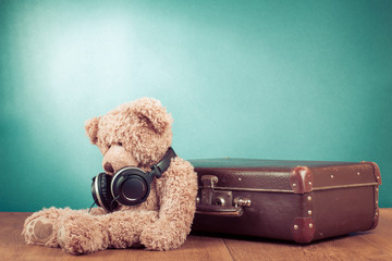 Retro teddy bear with headphones sitting near old suitcase