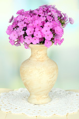 Beautiful bouquet of phlox in vase on table on light background