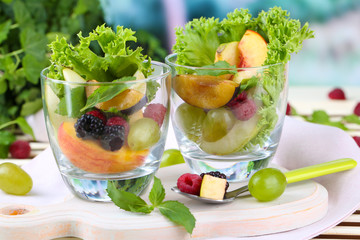 Fruit salad in glasses, on wooden table, on bright background