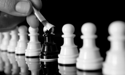 Close-up of a hand painting a black chess pawn white among white pawns, conceptual image...