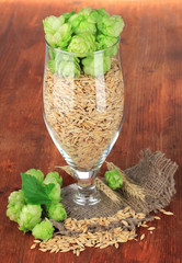 Glass of fresh green hops and barley, on wooden background