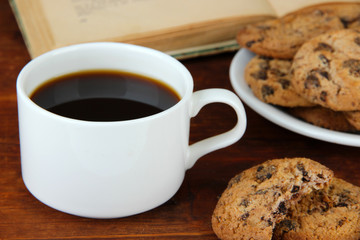 Cup of coffee with cookies and book on wooden background