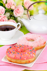 Sweet donuts with cup of tea on table on bright background