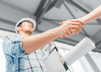 builder with blueprint shaking partner hand