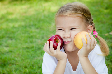 little girl sitting on the grass and holding apples