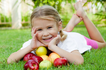 little girl lying on the grass and holding apples