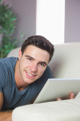 Content handsome man lying on couch using tablet