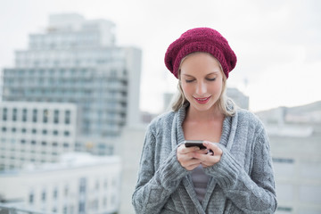 Smiling pretty blonde text messaging outdoors