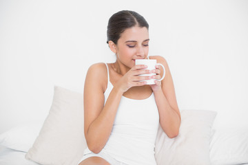 Calm young brown haired model in white pajamas enjoying coffee s