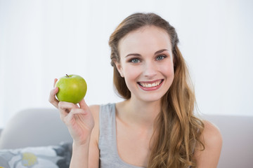 Happy young woman sitting on sofa holding green apple